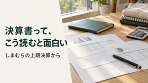 自然光の入る机で、決算資料と緑のノートを読む様子
